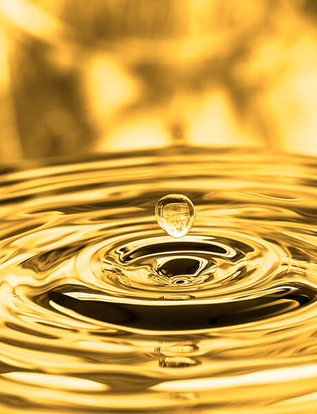 Golden water droplet hovering above rippling, gold-toned liquid surface.