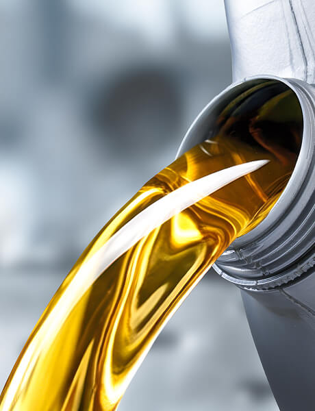 Close-up of golden oil pouring from a metal spout in an industrial setting.